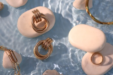 Photo of Different beautiful gold jewelry and rocks in water on light blue background, closeup