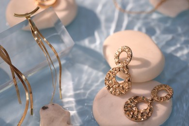 Photo of Different beautiful gold jewelry and rocks in water on light blue background, closeup