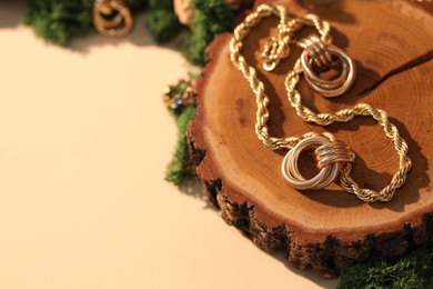 Photo of Beautiful gold jewelry and wood with moss on beige background, closeup. Space for text