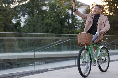 Photo of Happy man riding bicycle and waving to someone on city street. Space for text