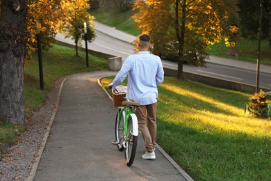 Photo of Happy man walking his bicycle in park on sunny day, back view