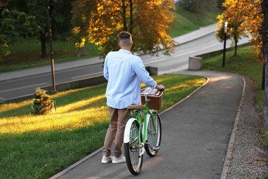 Photo of Happy man walking his bicycle in park on sunny day, back view