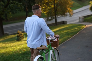 Photo of Happy man walking his bicycle in park on sunny day, back view