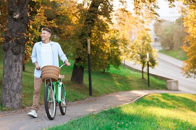 Photo of Happy man walking his bicycle in park on sunny day. Space for text