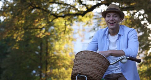 Photo of Happy man riding bicycle in park on sunny day. Space for text