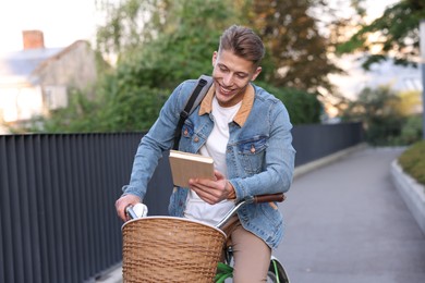 Photo of Happy man with book riding bicycle on city street