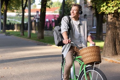 Photo of Happy man listening to music while riding bicycle in park. Space for text
