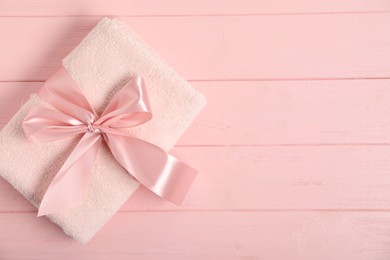 Photo of Fresh terry towel with bow on pink wooden background, top view. Space for text