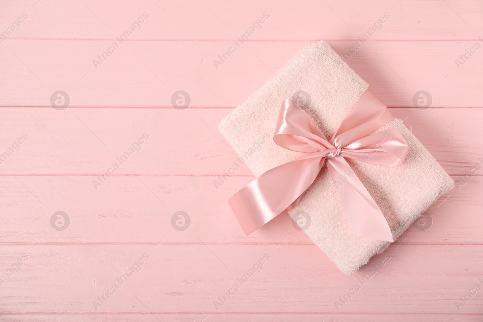 Photo of Fresh terry towel with bow on pink wooden background, top view. Space for text