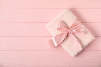 Photo of Fresh terry towel with bow on pink wooden background, top view. Space for text