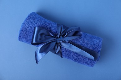 Photo of Fresh terry towel with bow on blue background, top view