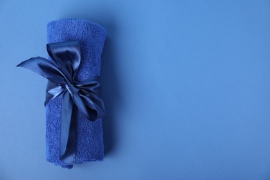 Photo of Fresh terry towel with bow on blue background, top view. Space for text
