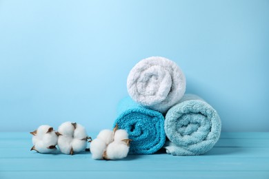 Photo of Fresh terry towels and cotton flowers on light blue background. Space for text