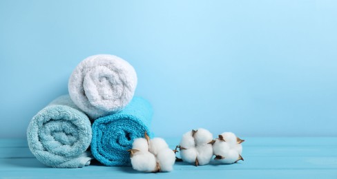 Photo of Fresh terry towels and cotton flowers on light blue background. Space for text