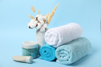 Photo of Fresh terry towels, personal hygiene products and cotton flowers on light blue background
