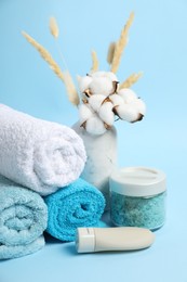 Photo of Fresh terry towels, personal hygiene products and cotton flowers on light blue background