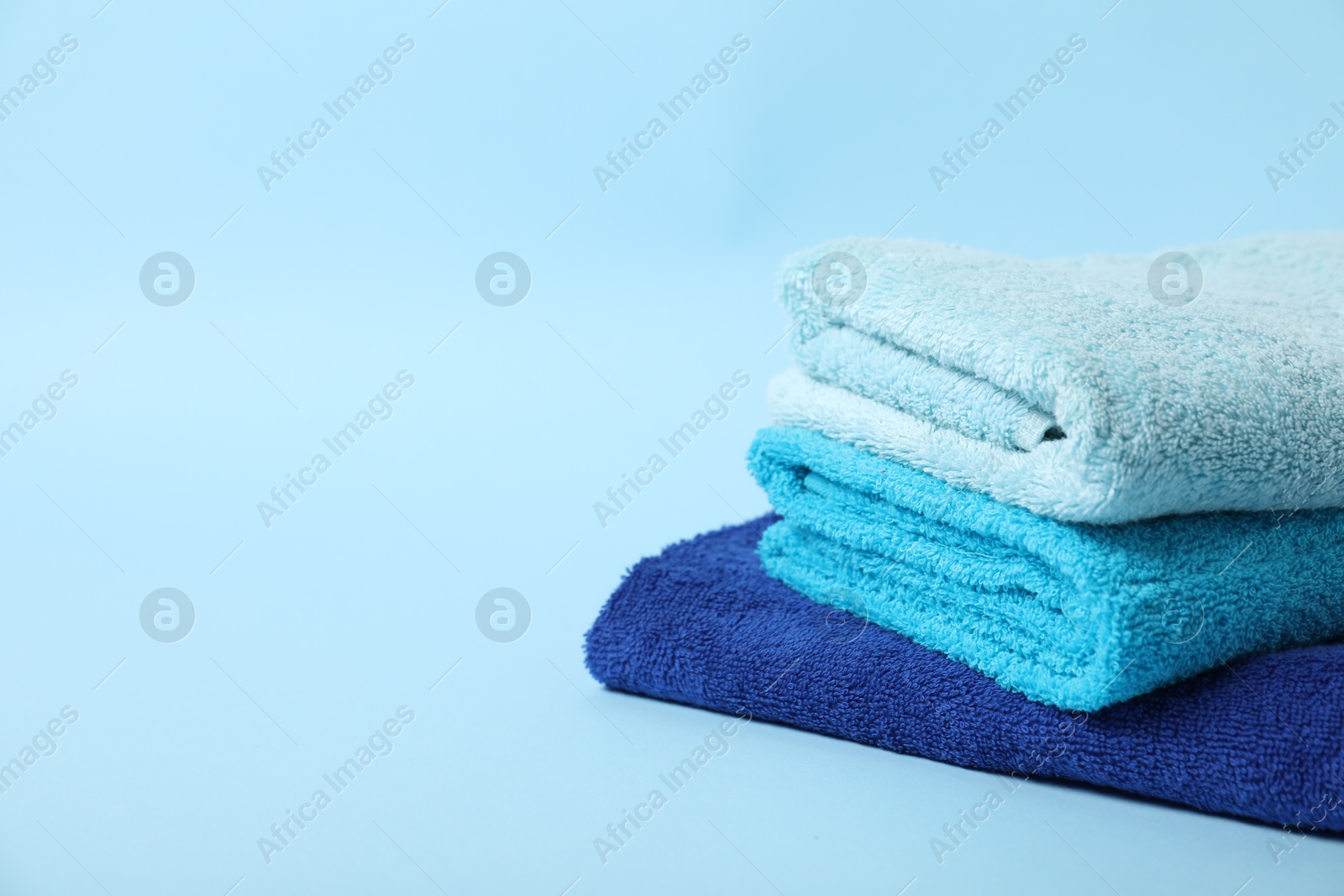 Photo of Stack of fresh terry towels on light blue background. Space for text
