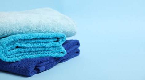 Photo of Stack of fresh terry towels on light blue background, closeup. Space for text