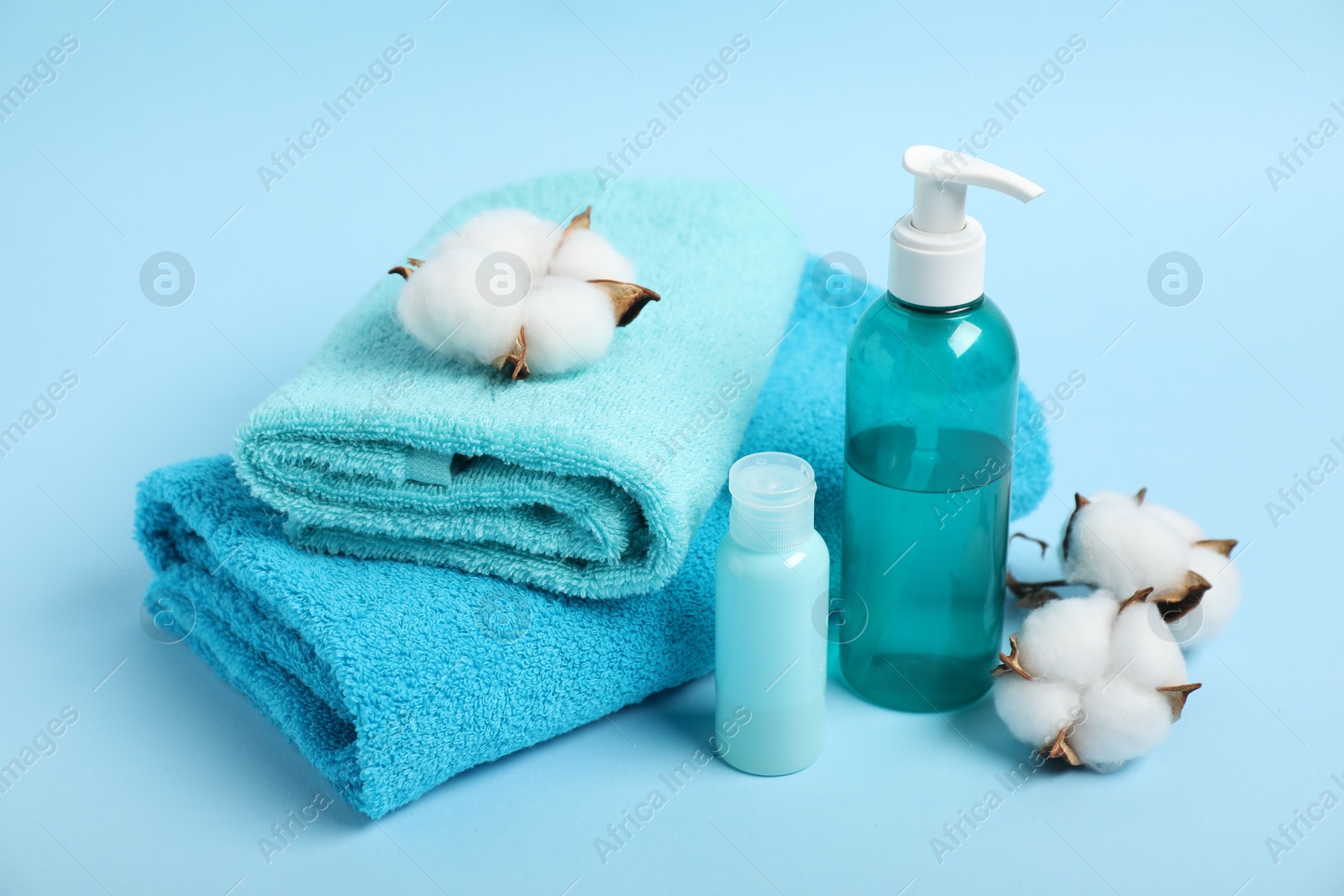 Photo of Fresh terry towels, personal hygiene products and cotton flowers on light blue background