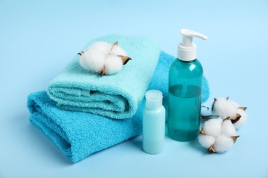 Photo of Fresh terry towels, personal hygiene products and cotton flowers on light blue background