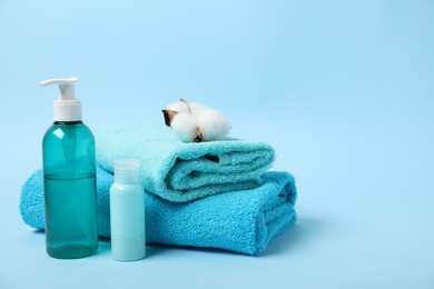 Photo of Fresh terry towels, personal hygiene products and cotton flower on light blue background. Space for text