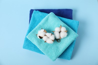 Photo of Fresh terry towels and cotton flowers on light blue background, top view