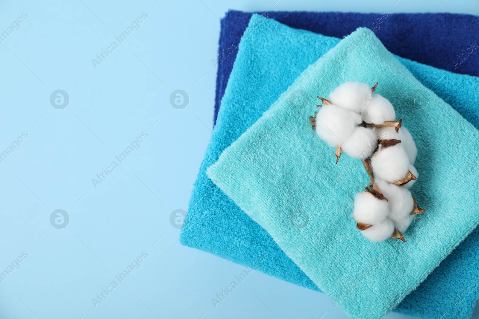Photo of Fresh terry towels and cotton flowers on light blue background, top view. Space for text