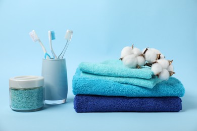 Photo of Fresh terry towels, personal hygiene products and cotton flowers on light blue background