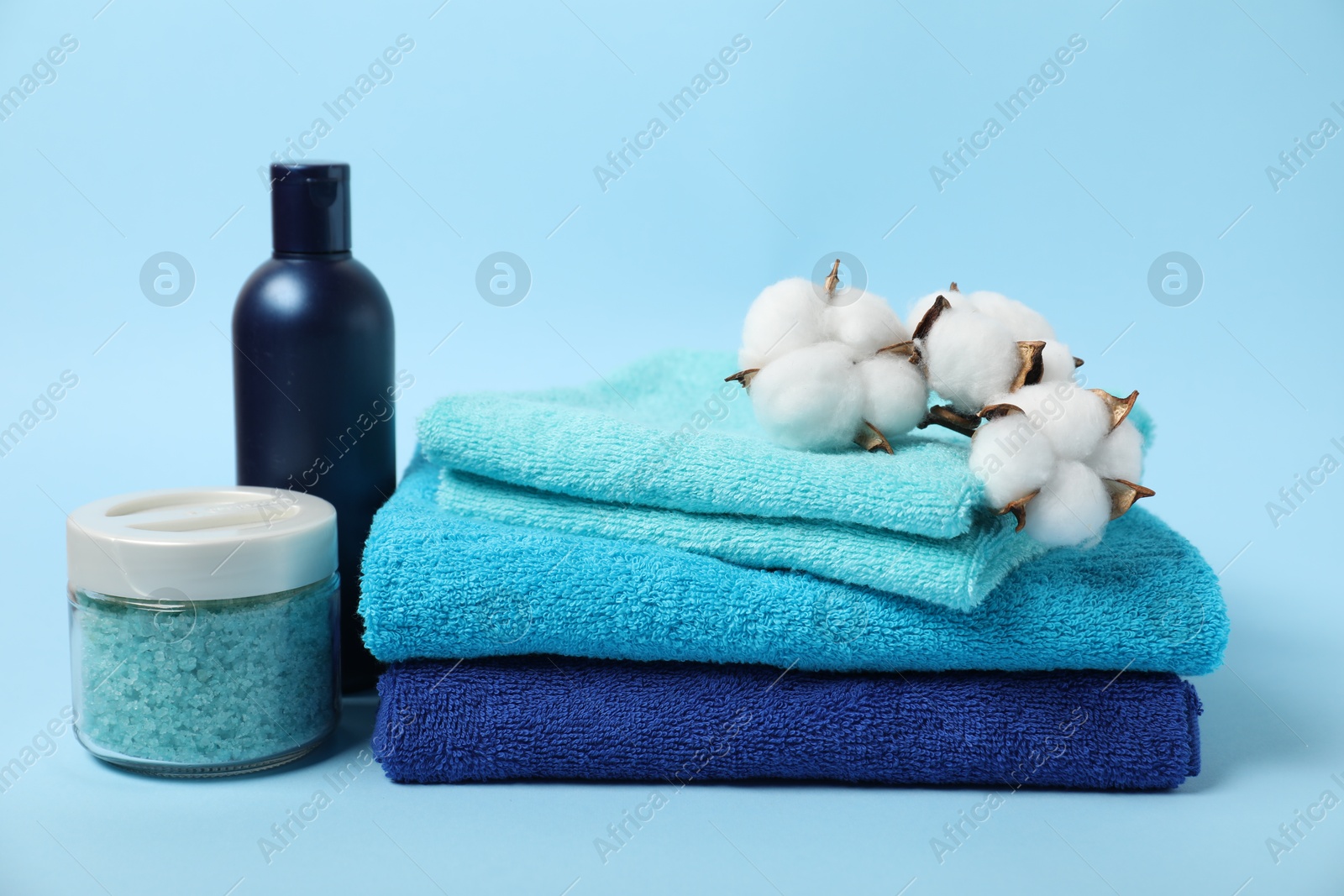 Photo of Fresh terry towels, personal hygiene products and cotton flowers on light blue background