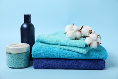 Photo of Fresh terry towels, personal hygiene products and cotton flowers on light blue background