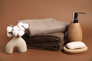 Photo of Fresh terry towels, cosmetic products and cotton flowers on brown background