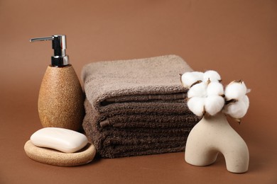 Photo of Fresh terry towels, cosmetic products and cotton flowers on brown background