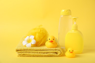 Photo of Fresh terry towel, cosmetic products and rubber ducks on yellow background