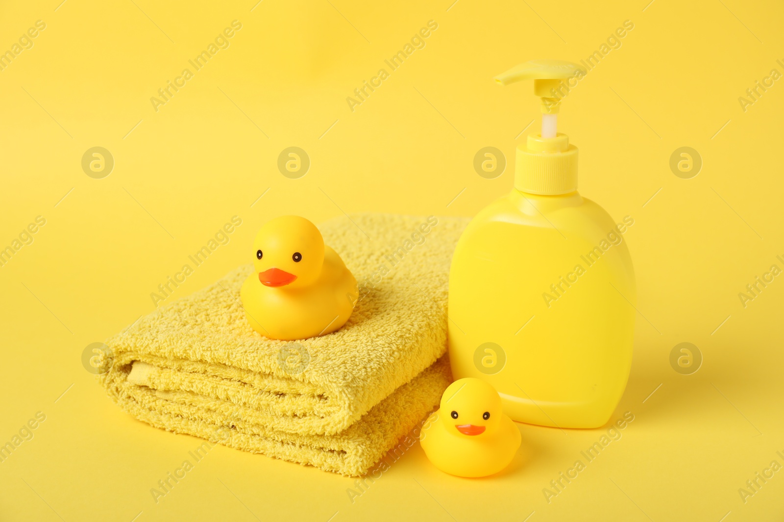 Photo of Fresh terry towel, cosmetic product and rubber ducks on yellow background