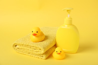 Photo of Fresh terry towel, cosmetic product and rubber ducks on yellow background