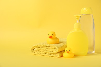Photo of Fresh terry towel, cosmetic products and rubber ducks on yellow background. Space for text