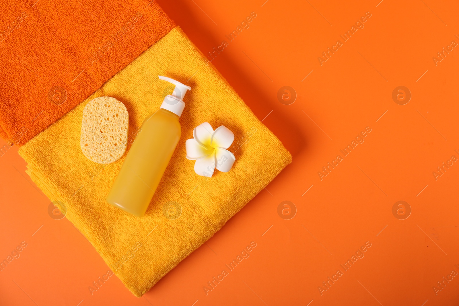 Photo of Fresh terry towels, sponge, flower and cosmetic product on orange background, top view. Space for text
