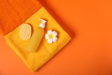Photo of Fresh terry towels, sponge, flower and cosmetic product on orange background, top view. Space for text