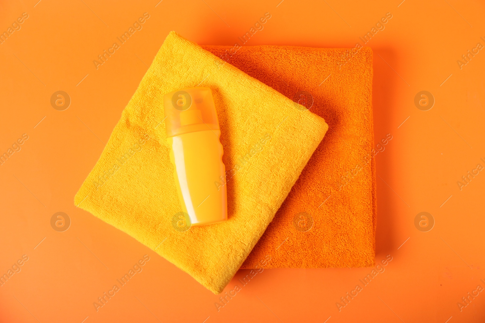 Photo of Fresh terry towels and cosmetic product on orange background, top view