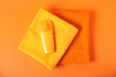 Photo of Fresh terry towels and cosmetic product on orange background, top view