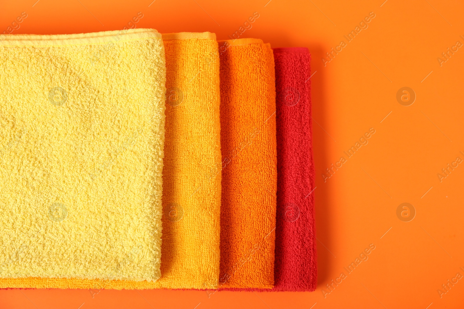 Photo of Fresh terry towels on orange background, top view