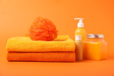 Photo of Fresh terry towels, cosmetic products and sponge on orange background