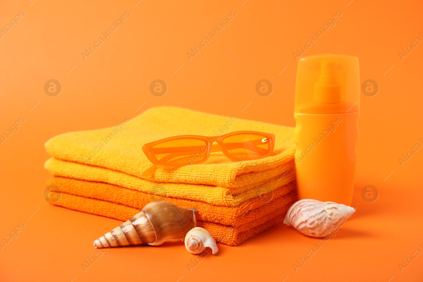 Photo of Fresh terry towels, cosmetic product, sunglasses and sea shells on orange background