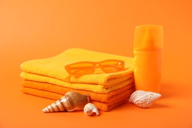Photo of Fresh terry towels, cosmetic product, sunglasses and sea shells on orange background