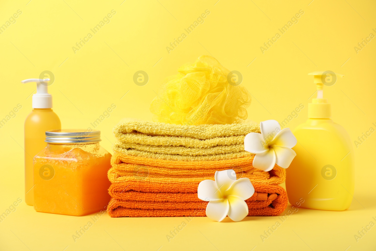 Photo of Fresh terry towels, cosmetic products, flowers and sponge on yellow background