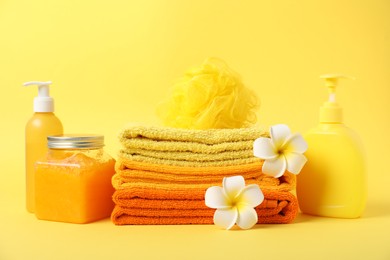 Photo of Fresh terry towels, cosmetic products, flowers and sponge on yellow background