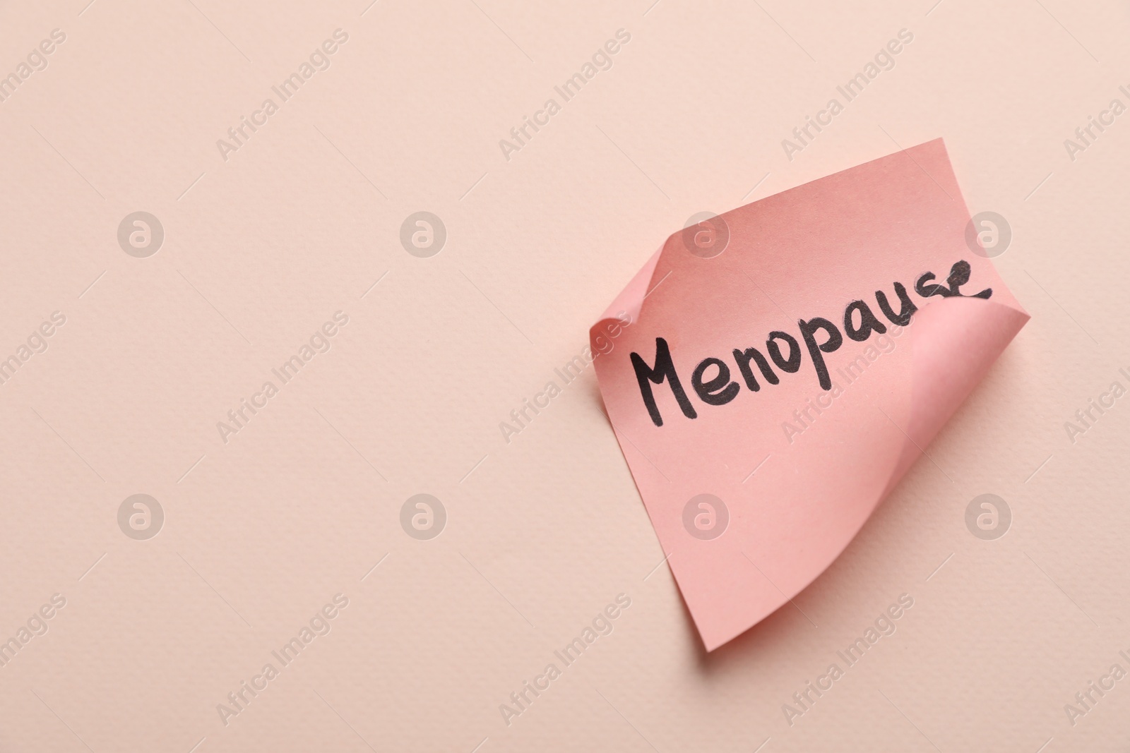 Photo of Paper note with word Menopause on beige background, closeup. Space for text