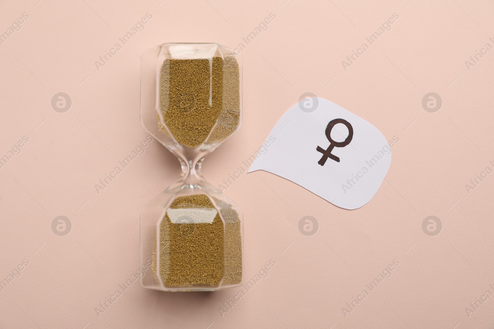 Photo of Menopause. Hourglass with female gender symbol on beige background, top view