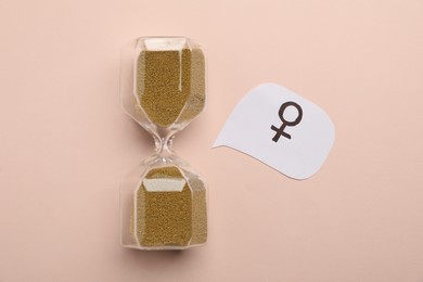 Photo of Menopause. Hourglass with female gender symbol on beige background, top view