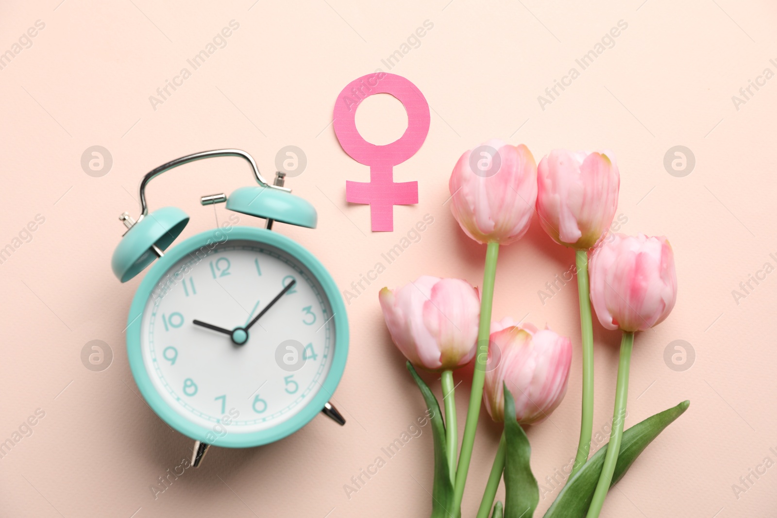 Photo of Menopause. Female gender symbol, alarm clock and tulips on beige background, flat lay